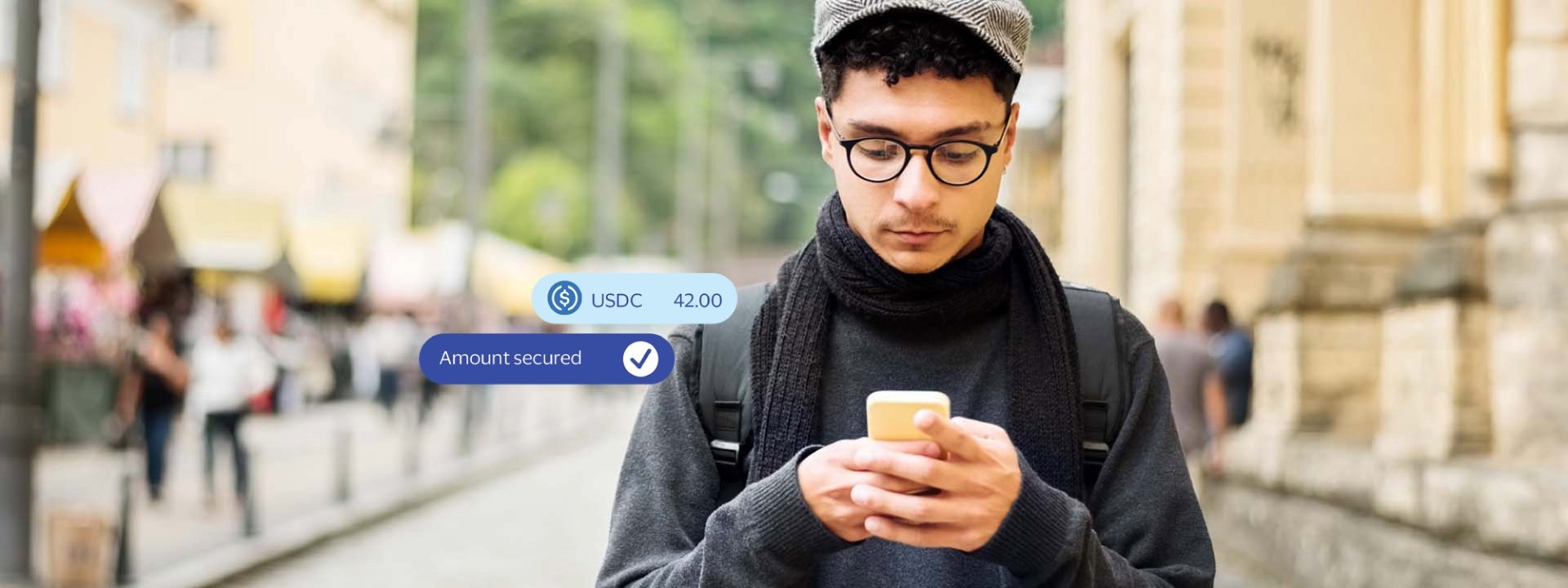 Young man walking down city street making a payment with a stablecoin-linked card on his mobile device