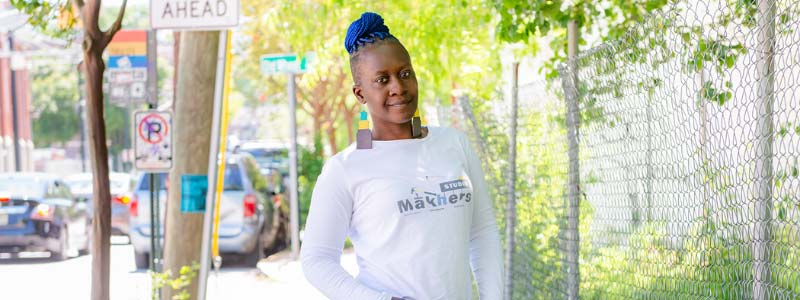 Image of woman standing outside in front of a fence with her hands in her pockets