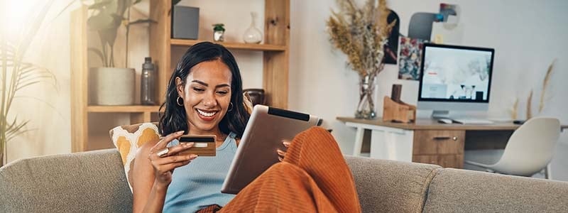 Smiling sitting on a couch looking at a credit card and tablet