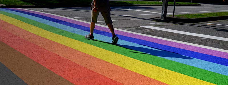 Person walking across a pride-inspired rainbow flag crosswalk.