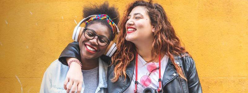 two women with arms around each other in front of yellow wall