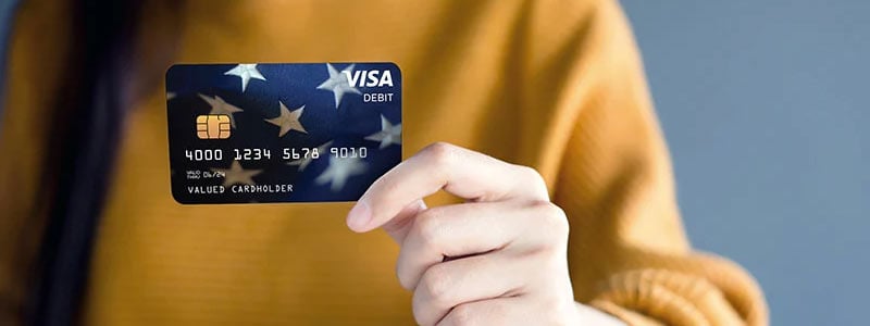 Person wearing a yellow sweater holding out a Visa card.