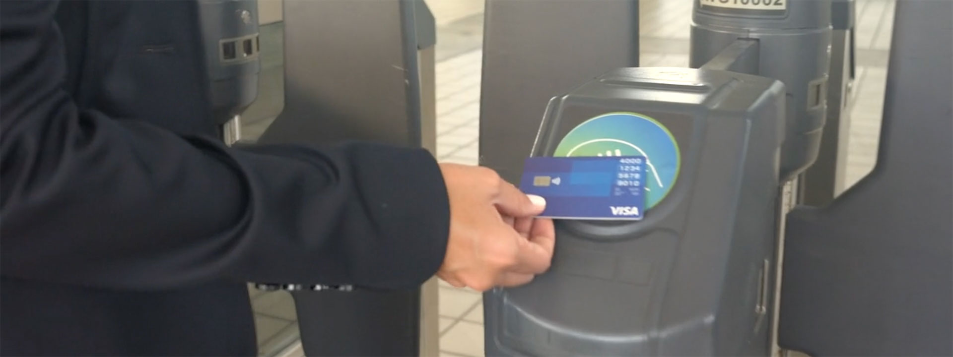 Hand holding a contactless Visa card at a transit point of sale terminal.