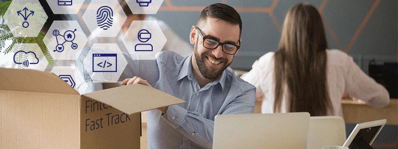 smiling man in office looking at laptop on desk and unpacking box