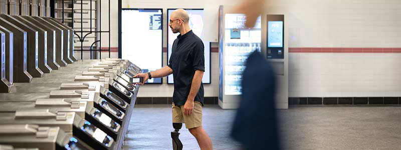 Man with a prosthetic leg taps his payment-enabled device to enter a subway station