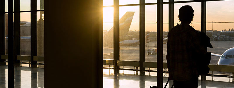 silhouette of passenger looking out airport window onto tarmac