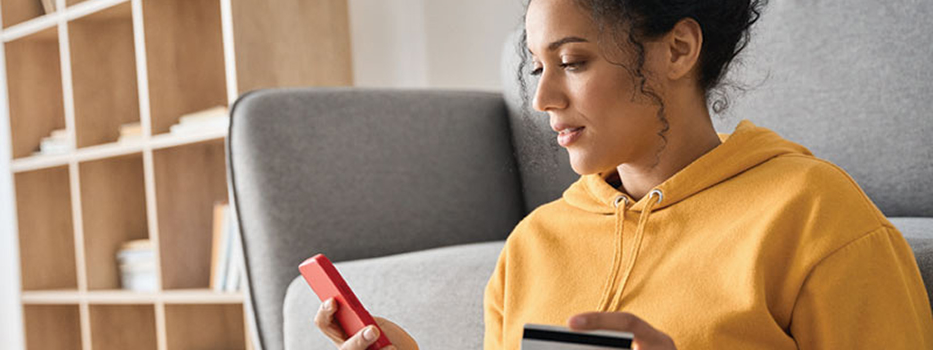 woman wearing yellow hoodie entering her card information into her smartphone