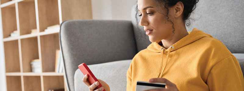 woman wearing yellow hoodie entering her card information into her smartphone