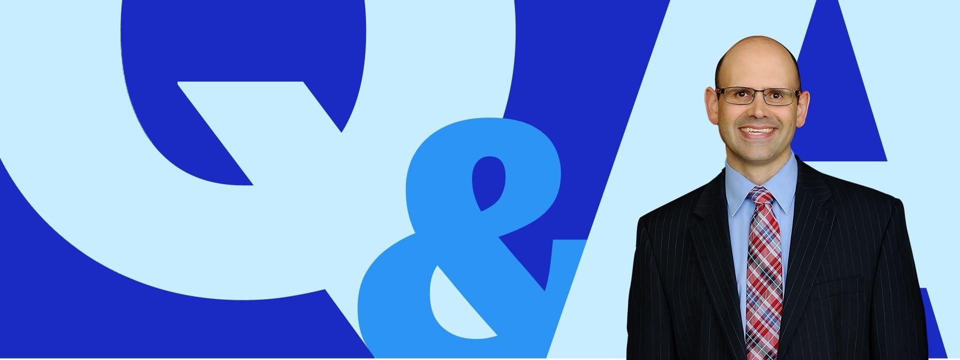 Professor Jim Hawkins in a suit and tie, smiling in front of a bold blue ‘Q&A’ graphic on a light blue background.