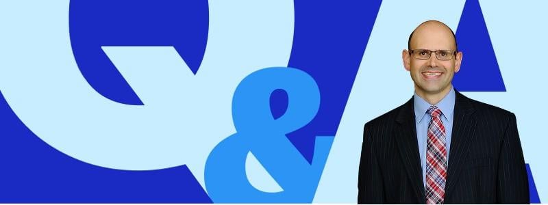 Professor Jim Hawkins in a suit and tie, smiling in front of a bold blue ‘Q&A’ graphic on a light blue background.