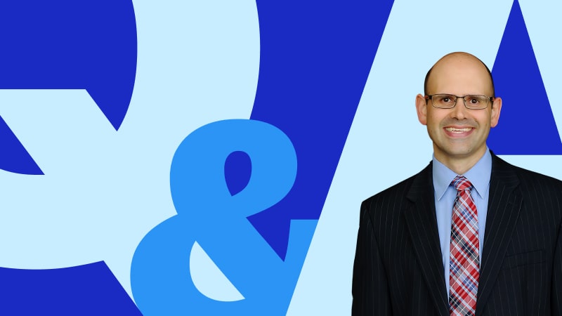 Professor Jim Hawkins in a suit and tie, smiling in front of a bold blue ‘Q&A’ graphic on a light blue background.