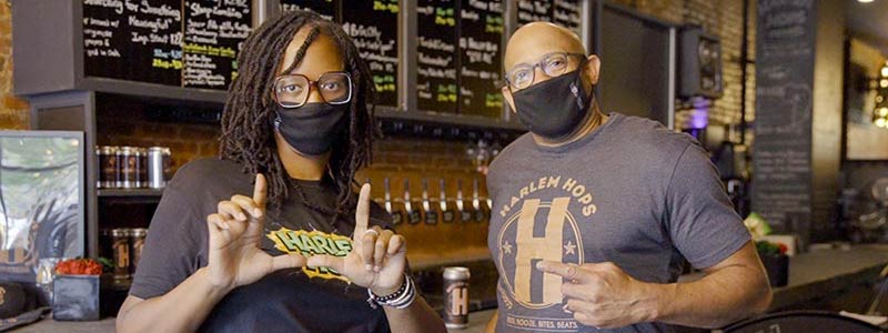 A woman and a man in COVID masks pose in front of a bar.