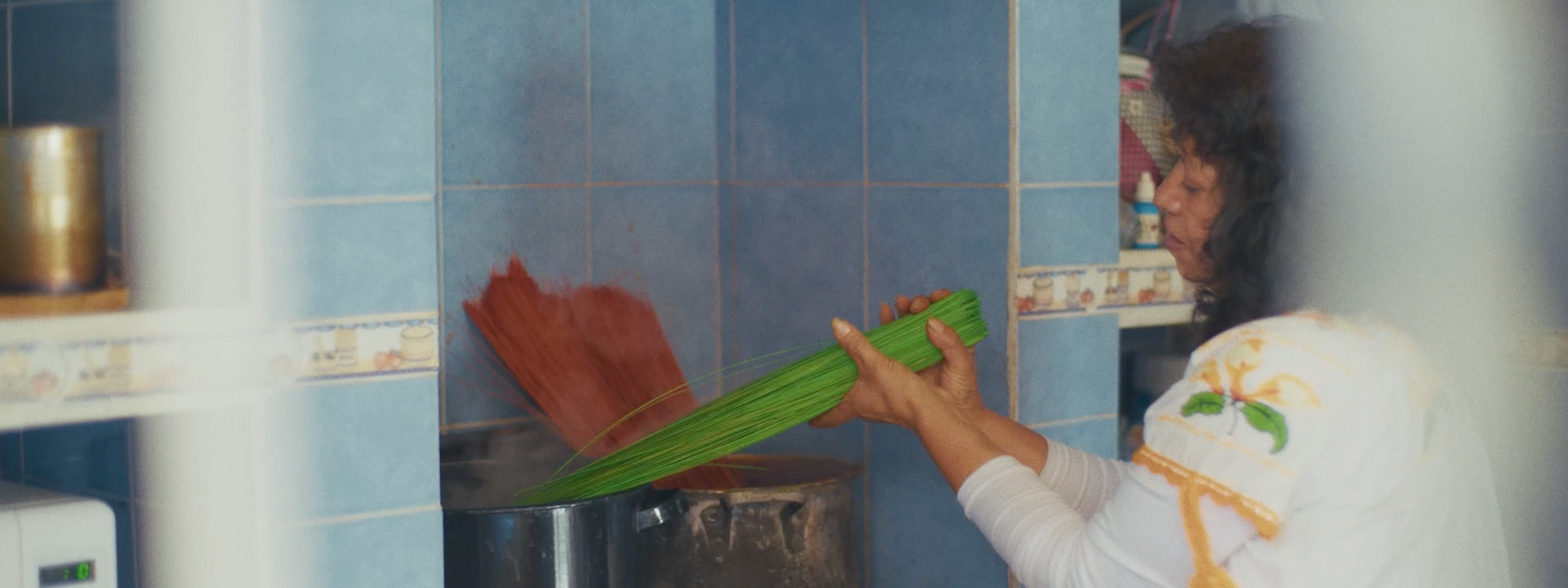 Woman dying bunches of poptillo green and red in big pots on a stovetop.