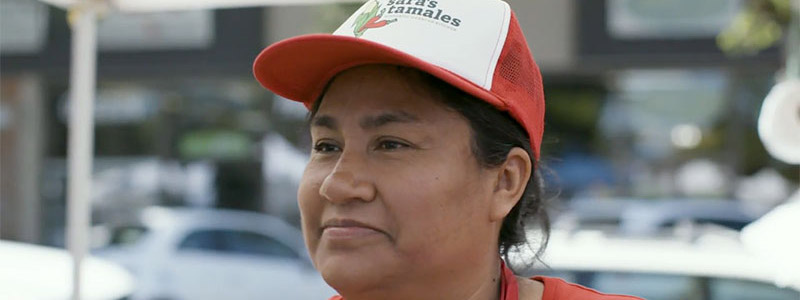 Small business owner Sara Rodriguez smiles off camera wearing a hat with her company's logo.