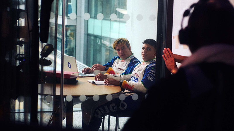 VCARB drivers sit at a desk in a small conference building in front of a video production team.