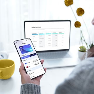 Person looking at transaction details on their phone at their desk. Visa logo can be seen on digital card in mobile screen.