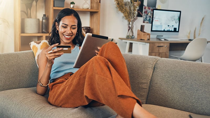 Smiling sitting on a couch looking at a credit card and tablet