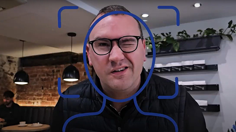 A man with glass squinting one eye as the video camera focuses and creates a blue outline
