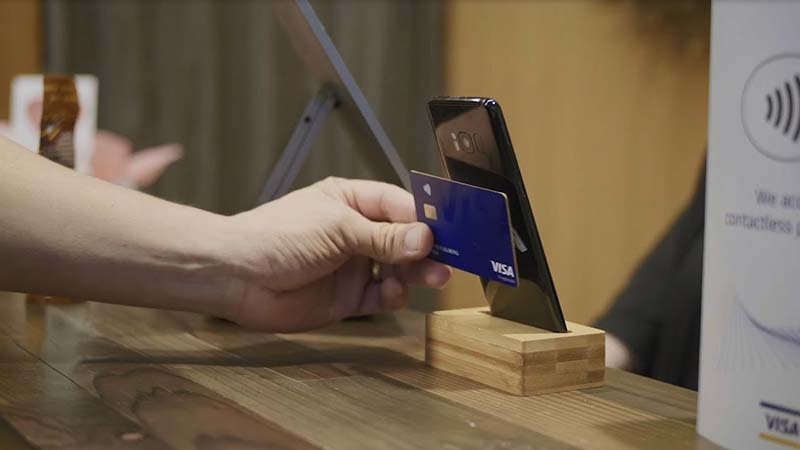 Hand holding a card to the back of a phone for a contactless transaction.