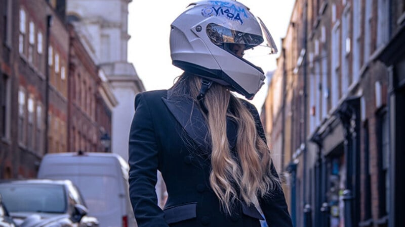 Team Visa skateboard athlete Sky Brown standing in the middle of a street holding a skateboard and wearing a Visa-branded F1 helmet.