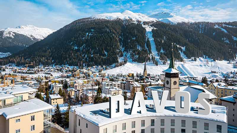 View of Davos, Switzerland with snow-covered buildings in the foreground and mountains in the background.