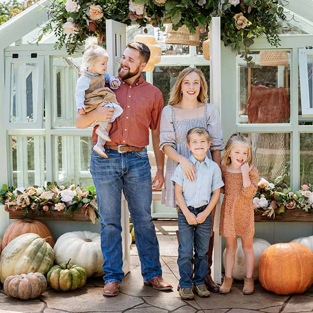 Small business owner, Kaylee Koch, stands with her smiling family in front of a floral arch