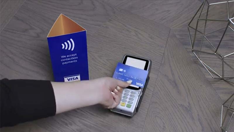 Hand holding a contactless payment card to a point of sale terminal.