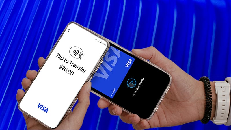 Two hands hold smartphones; one displays " Tap to Transfer $20.00" and the other a Visa card