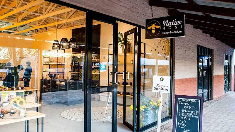 Exterior of the Native Nosi Honey Emporium, with open doors, product displays, and a chalkboard advertising an opening special.