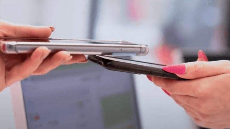 Two people hold smartphones close together for contactless payment, one with bright pink painted nails.