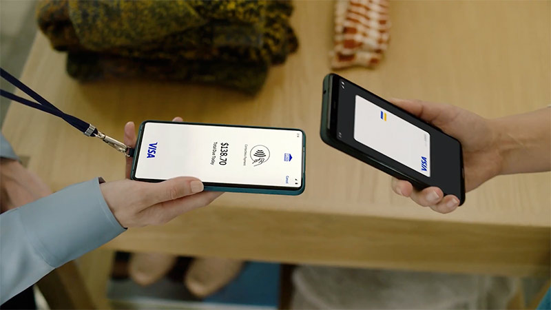 Shopkeeper holds out a phone while customer taps their phone to complete the transaction.