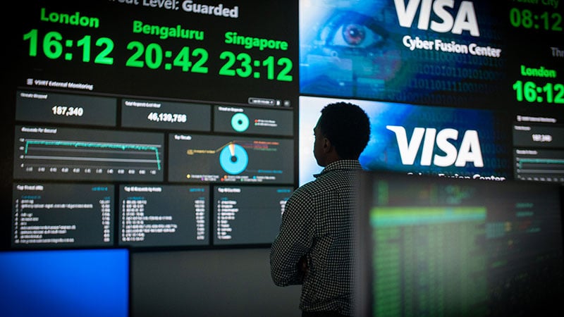 Employee stands in front of a wall of screens displaying payments dashboards at the Cyber Fusion Center.