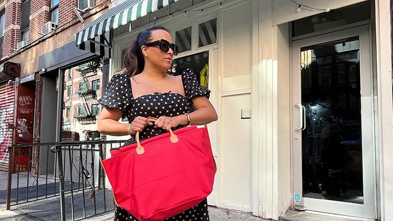 Woman wearing polka dot dress holding red bag standing on a street in New York City.