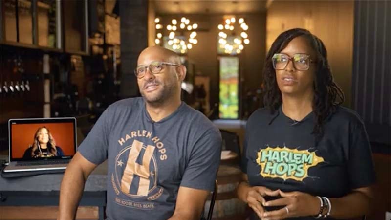 Man and woman sitting in a bar talking to the camera.