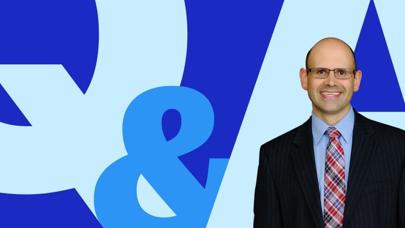 Professor Jim Hawkins in a suit and tie, smiling in front of a bold blue ‘Q&A’ graphic on a light blue background.