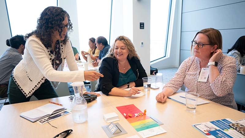 One waman teaching two other woman at a table in a conference room