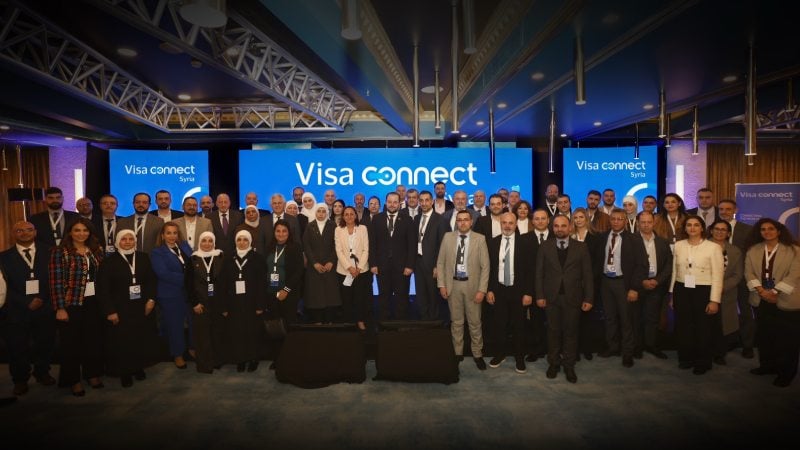 Group photo of diverse adults in business attire at a conference, standing in front of a blue "Visa Connect" backdrop. The atmosphere is professional and collaborative.