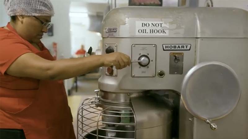 Woman wearing a hair net using a mixer in a commercial kitchen.