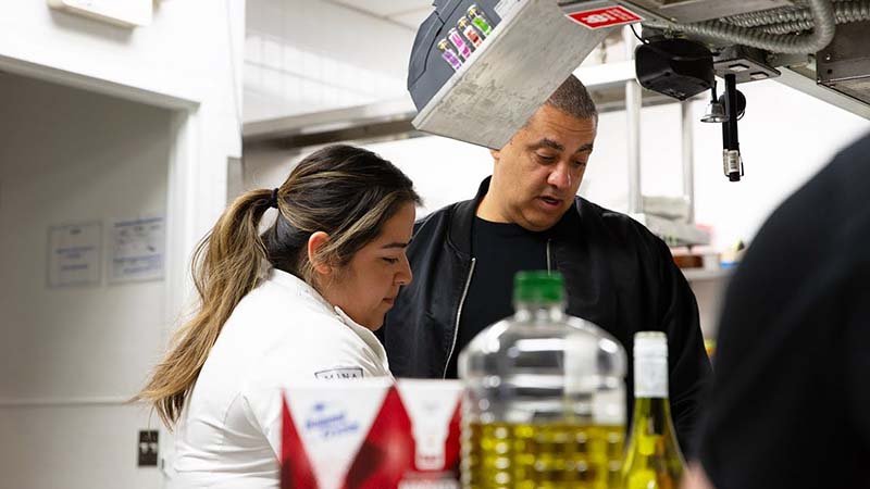 Chef Michael Mina talks to an employee in a restaurant kitchen.