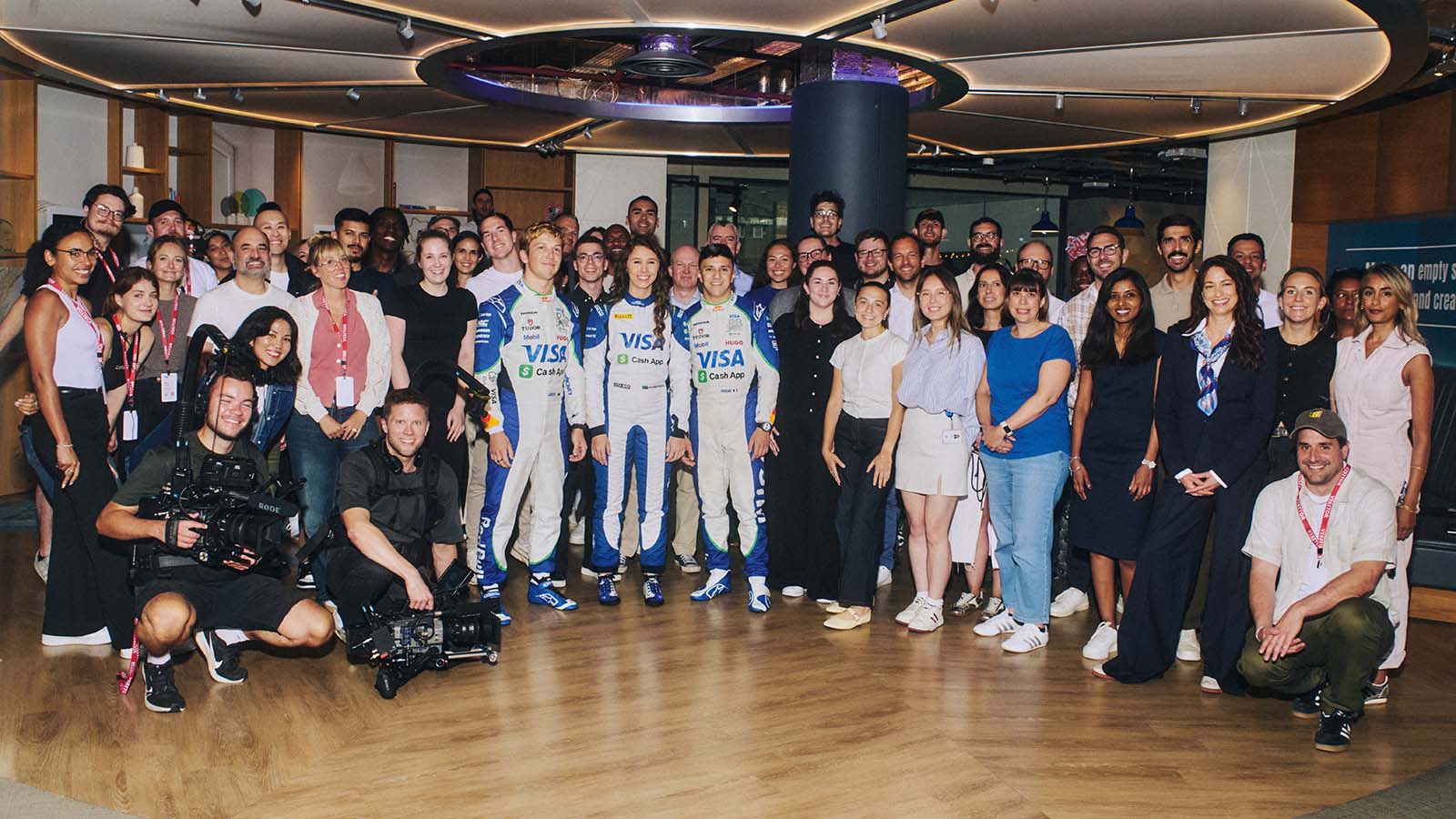 Drivers, employees and the video production crew stand in line in the office posing for a photo.