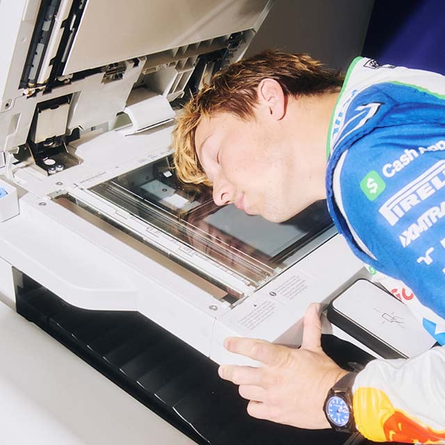 Driver Liam Lawson resting his head on an open photocopy machine.